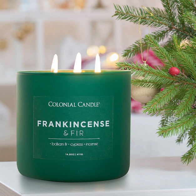 Green candle labeled 'Frankincense & Fir' next to a Christmas tree with ornaments.