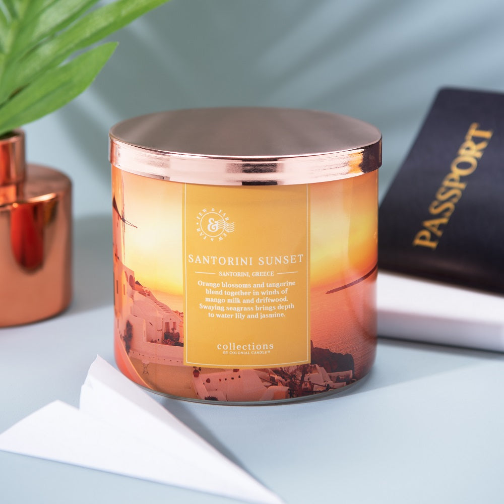Candle labeled 'Santorini Sunset' with a scenic design on a light blue surface.