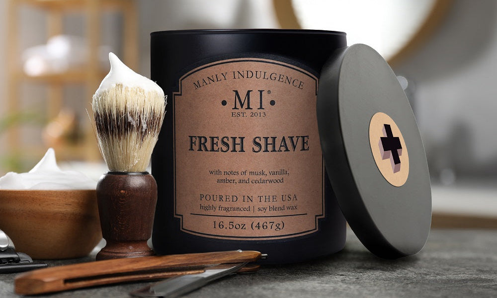 Manly Indulgence Fresh Shave candle with shaving brush and accessories on a table.