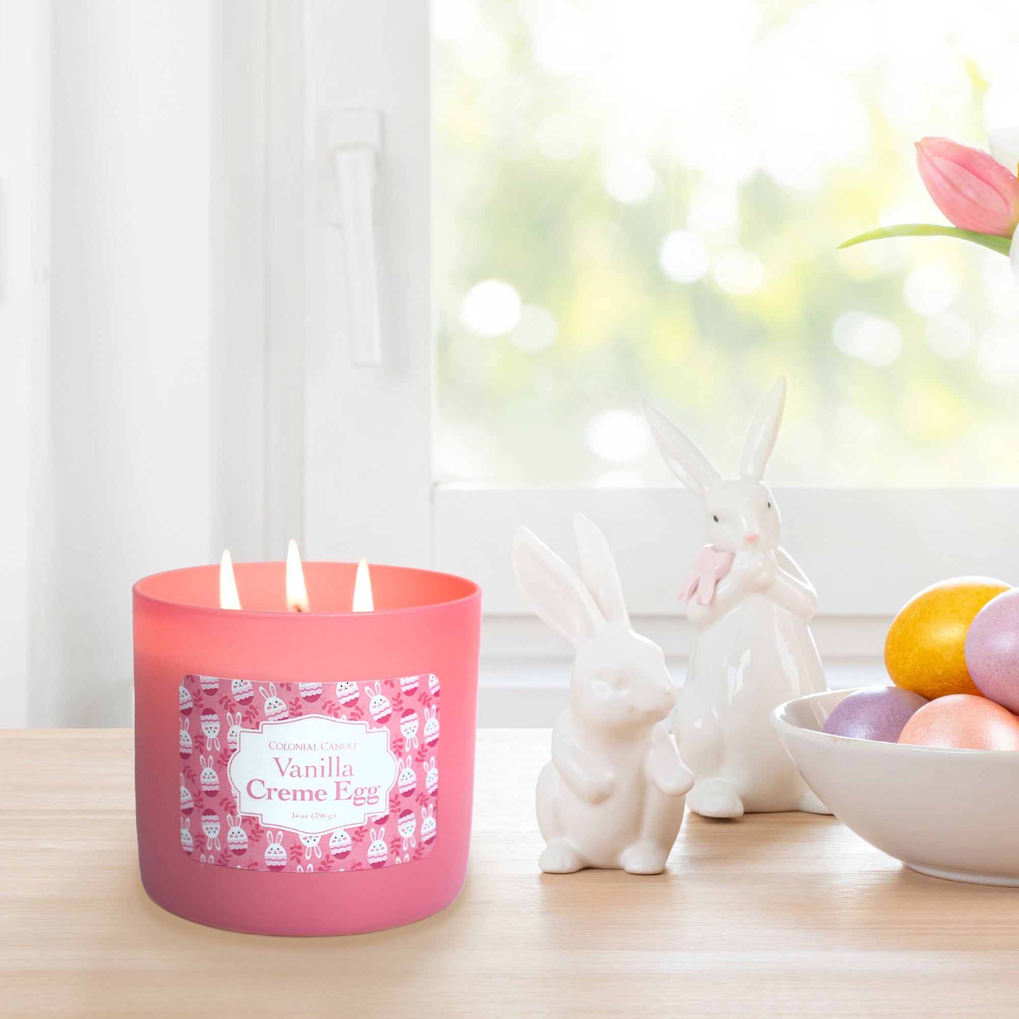 Pink candle labeled 'Vanilla Creme Egg' with decorative eggs and rabbit figurine on a light background