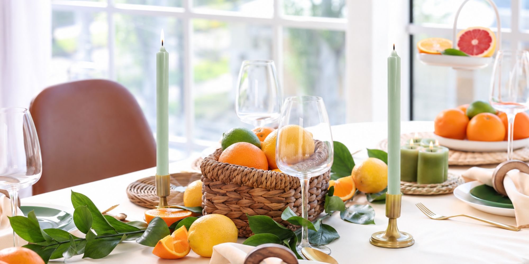 Decorative table setting with fruits, candles, and glasses on a white tablecloth.